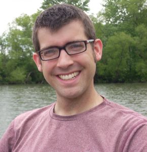 A man smiling widely in front of a pond