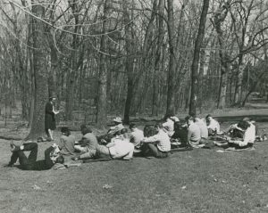 Black and white photograph of a woman teaching outside to a group of students