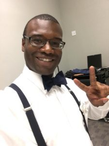 Picture of the author dressed in bowtie, white shirt, and suspenders smiiling and making the peace sign