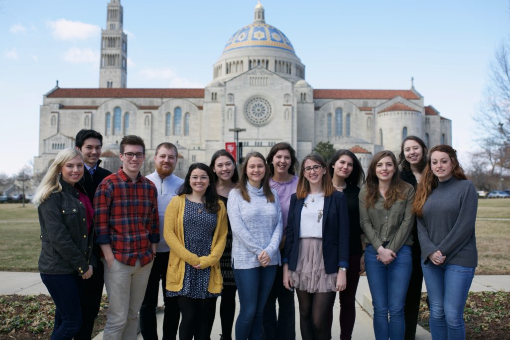 The 2017-18 Inventio Student Editorial Board pose together in front of a large stone building with an ornate light blue and yellow domed roof.