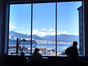 Shadows of people look out towards the outline of distant mountains through a large series of windows.
