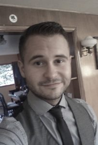Mike Haen smirks in a black tie and vest.