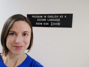 Karen Best smiles in front of the Program in English as a Second Language room sign.