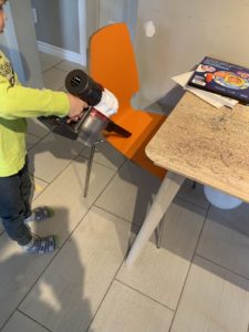 A boy attempts to vacuum up glitter around a children's table and chair using a hand vacuum.