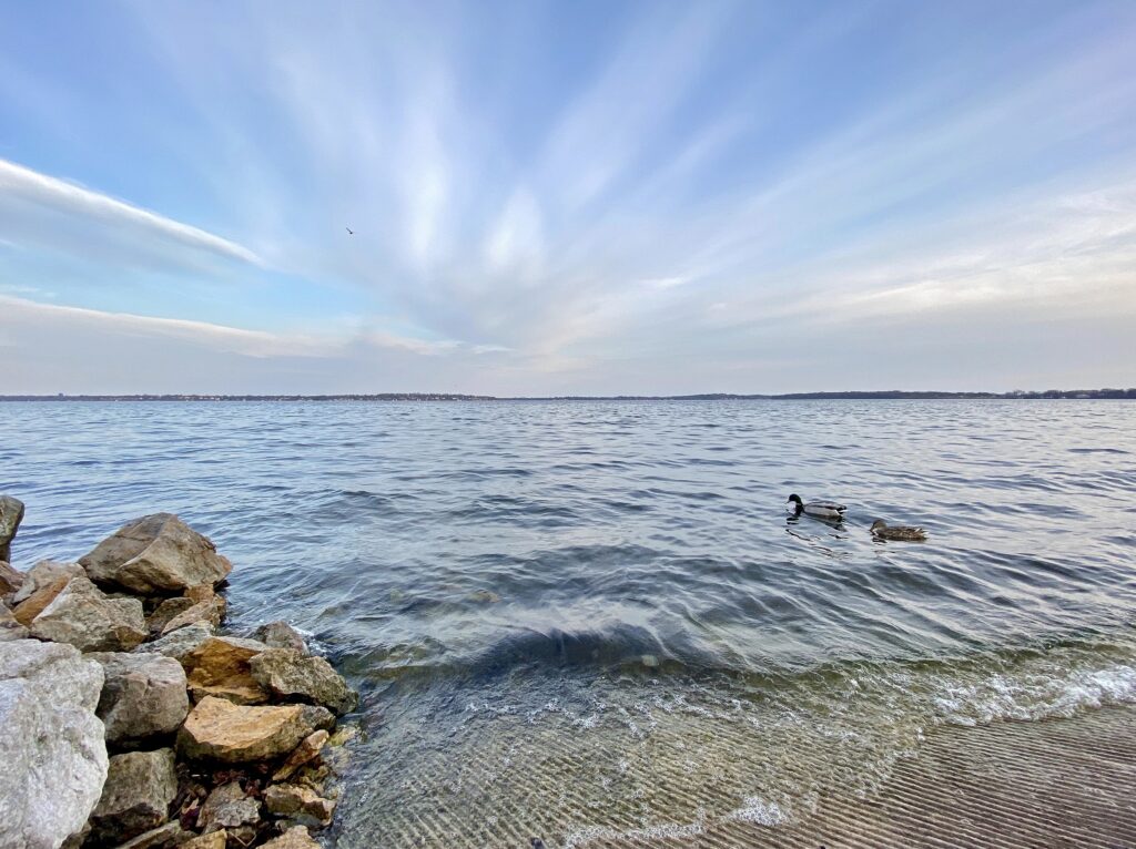 image shows Lake Monona, a blue sky with some wispy clouds overhead, and waves breaking in the foreground