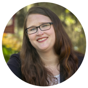 A white woman in her early thirties with brown hair and glasses.