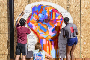 UW-Madison students (left to right) Daniel Ledin, Molly Pistono, and Courtney Gorum work together to paint a mural of a colorful fist commemorating the names of Black victims of police violence and racial injustice 