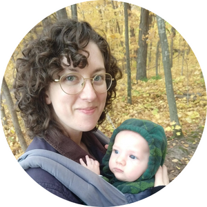 Zoe Cohen with her infant strapped to her front in a fall woods setting.