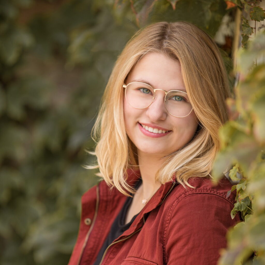 Emily Wesoloski wearing glasses and leaning against an ivy covered wall