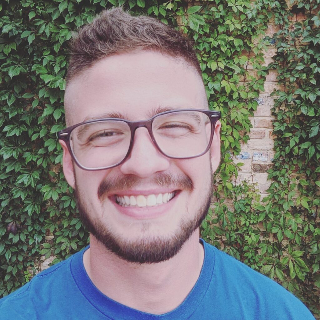 Jett Bailey smiling widely at the camera in front of an ivy covered wall