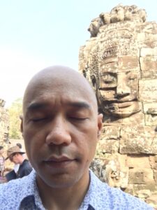 A man meditates before a large Buddha statue amidst a busy crowd.