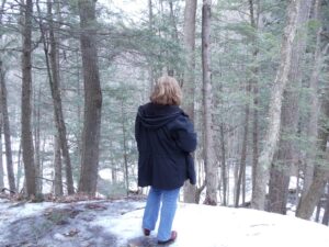 A woman gazes out over a snowy wooded area.