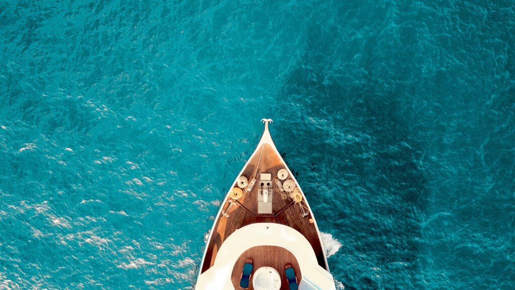 A boat's prow, viewed from overhead, slices through turquoise water.