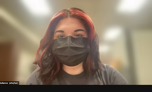 A screenshot of Julianna on Zoom. She is wearing a black surgical mask and has her name and pronouns visible on Zoom.