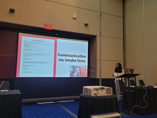 Samitha Senanayake standing in a conference room in front of a display screen that says "Communication via Intake Form"