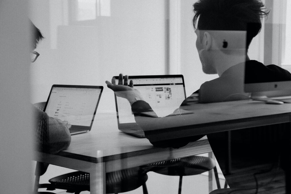 two people's backs sitting and working in front of their laptops.