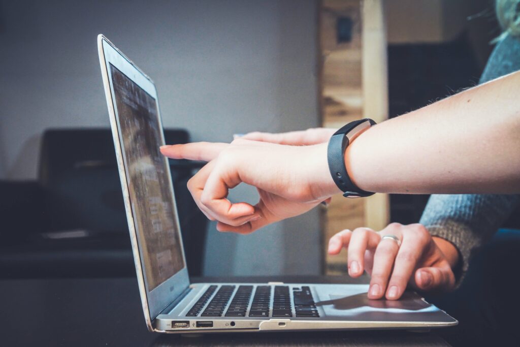 a person's hand pointing at the screen of a laptop