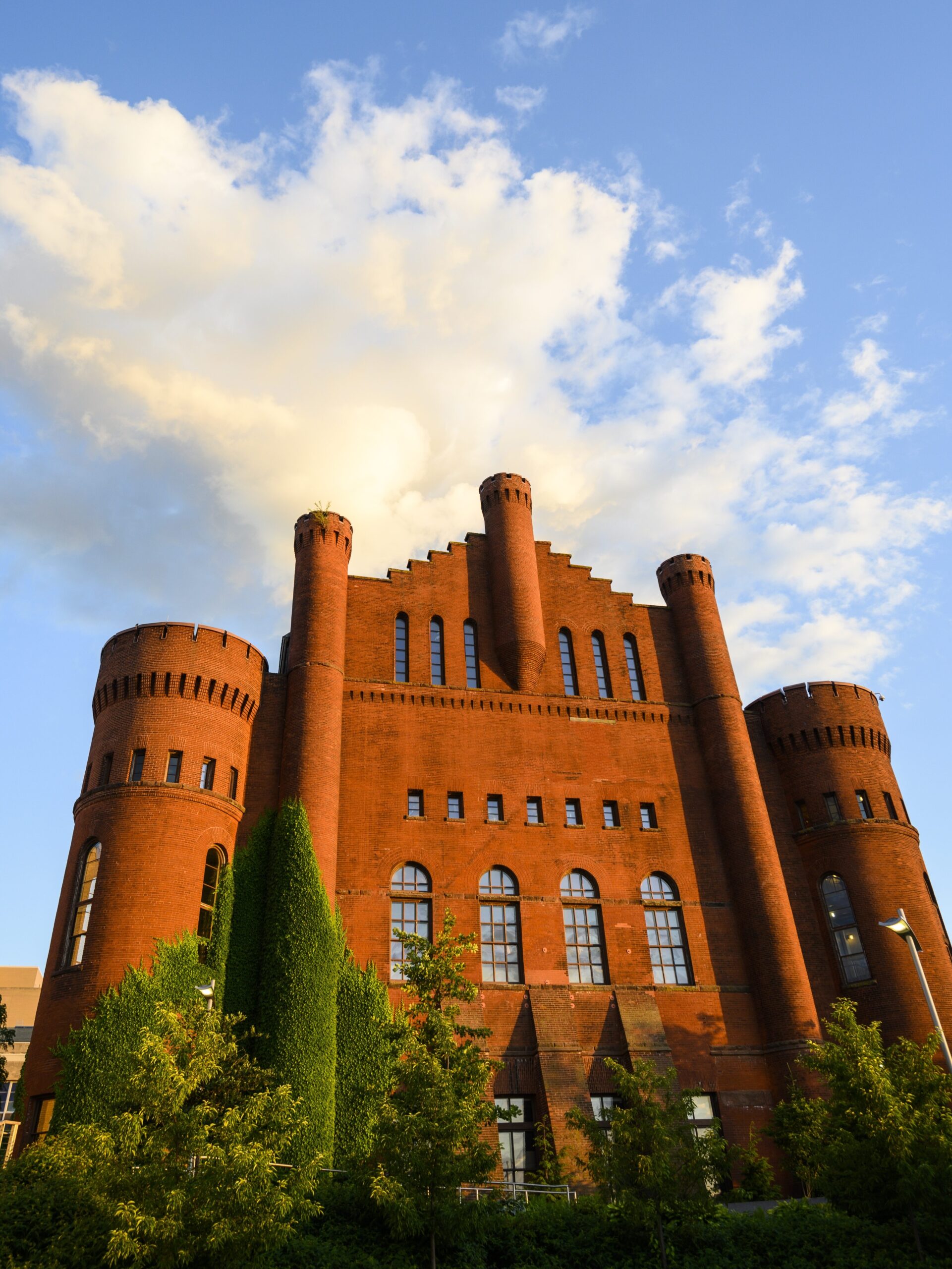 Red brick building that appears castle like with green trees in front of it.