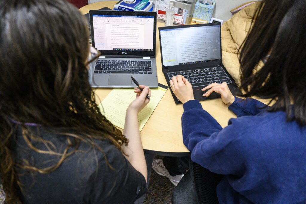 Two individuals sitting at a table with laptops in front of them