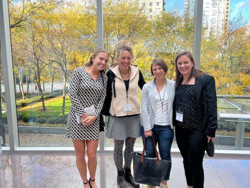 Authors Susanne and Karen with two other conference participants. They are standing in front of a large window overlooking a park.