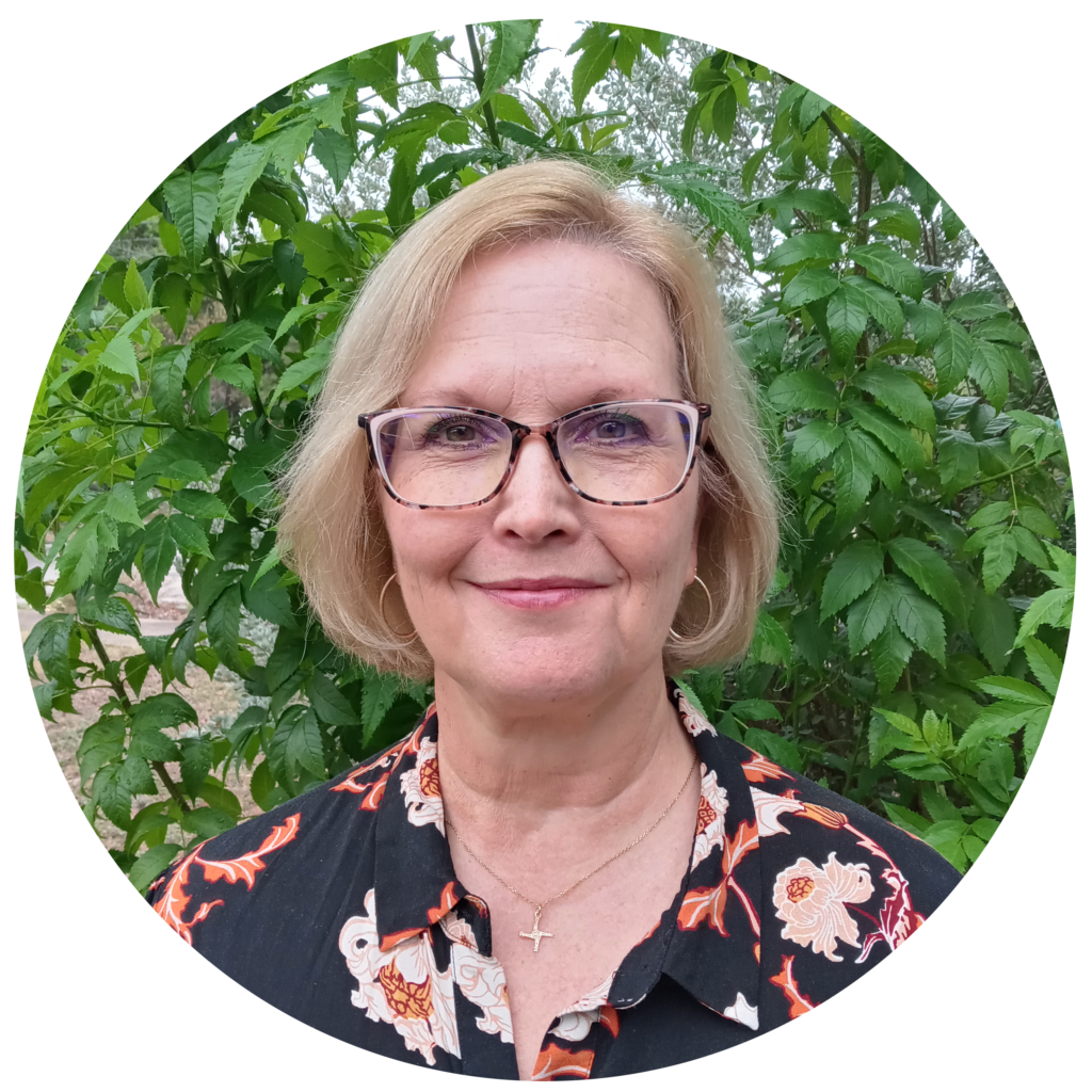 Nancy Effinger Wilson wearing glasses and smiling in front of some outdoor greenery