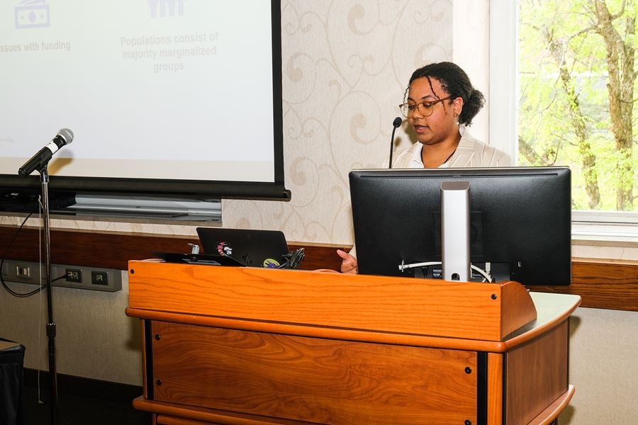 A Black woman stands behind a podium and is speaking into a microphone.