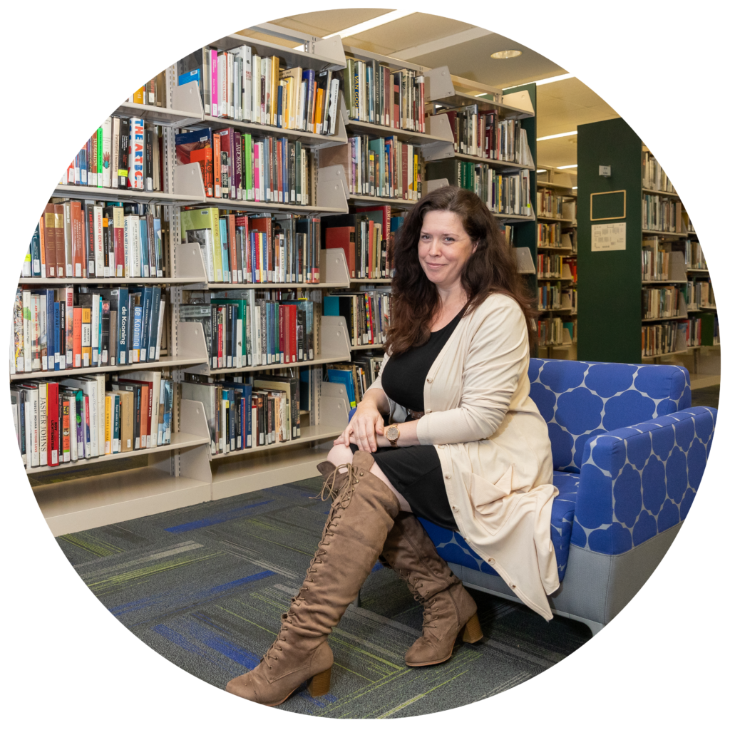a caucasian woman with brown hair seated on a blue chair in a library