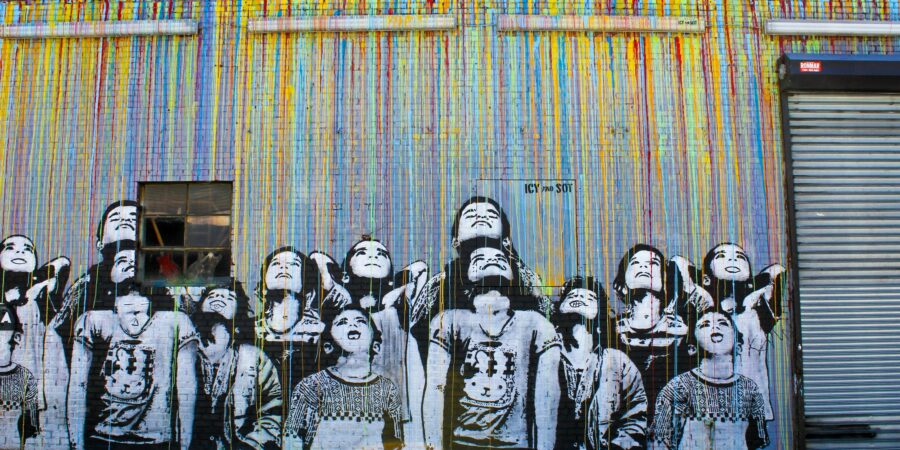 Street art of black and white children looking up with streams of colorful paint falling towards them.
