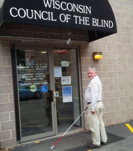 Tim Davis enters the building with a smile on his face and a cane in hand. The awning reads "Wisconsin Council of the Blind and Visually Impaired." 